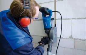 Мастер по электромонтажу выполняет штробление стен в квартире под проводку