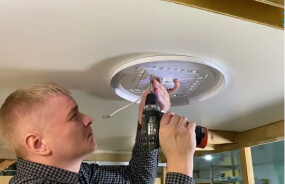 Мастер производит установку светильника на потолке
